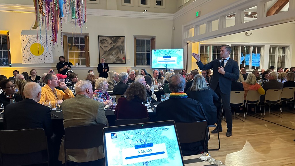 Ethan Merrill calling the live auction, with the pledge total on the screen behind him.