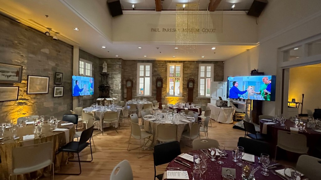 Round tables in the Paul Paresky Museum Court, with matching program screens on two walls.