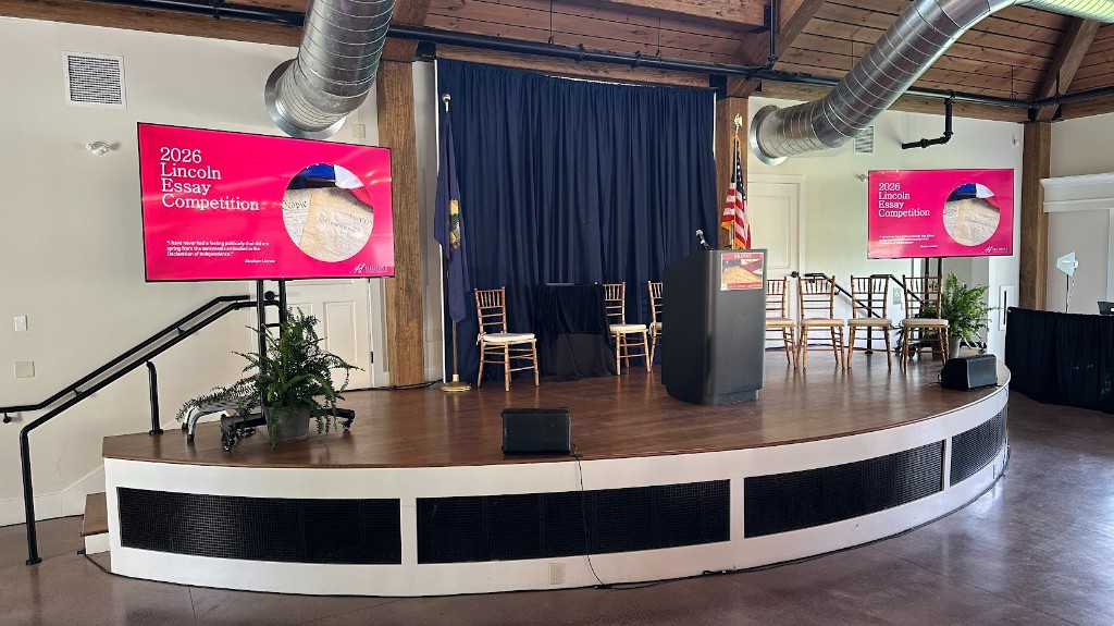 Wide view of Lincoln Hall at Hildene set for the Lincoln Essay Competition awards luncheon, red tablecloths, three screens in position.