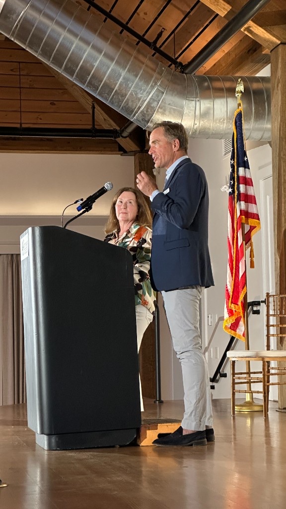 Craig Gemmell speaking at the podium in Lincoln Hall, with Christine Furman looking on.