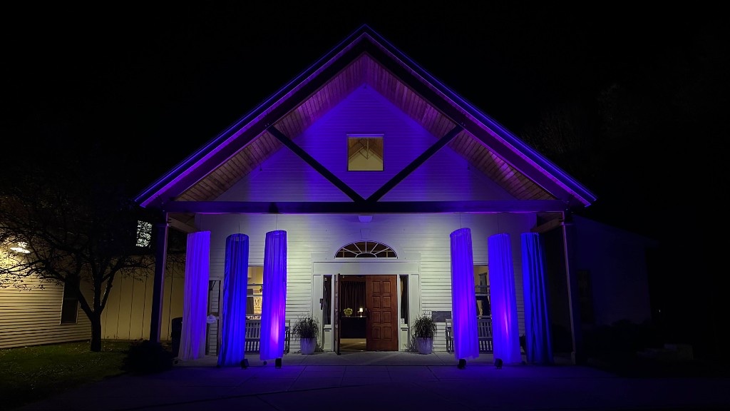 The front of Maple Street School at night, white drapes and purple uplights on the gable.