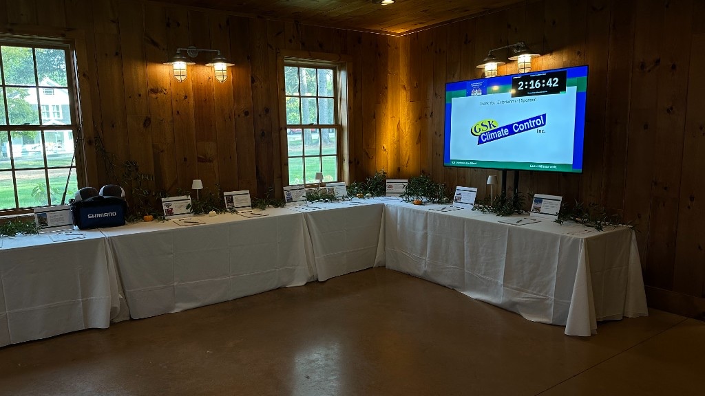 Silent auction tables under a 75-inch showing a sponsor thank-you and the countdown.