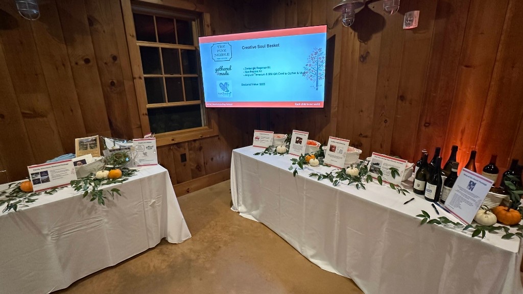 Silent auction tables under a 75-inch showing a Creative Soul Basket lot.