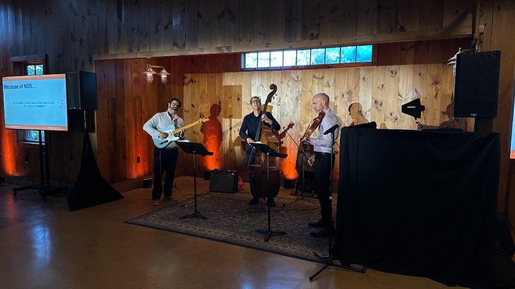 Northwoods Jazz Trio on the floor of the Celebration Barn, flanked by 75-inch displays and two ellipsoidals.