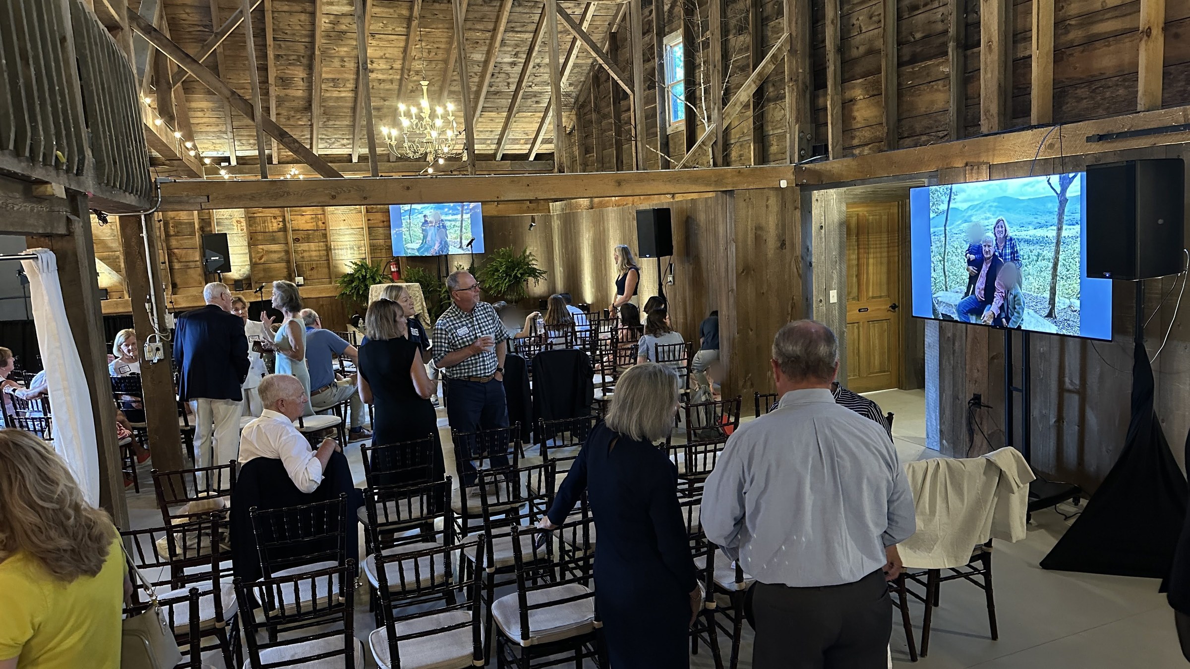 Guests gathering in The Old Gray Barn with 75-inch monitors, speakers, and warm perimeter uplighting.