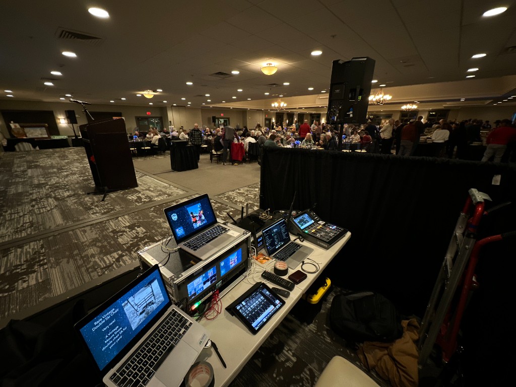 The tech table: playback laptops, a switcher, and a speaker on a stand.