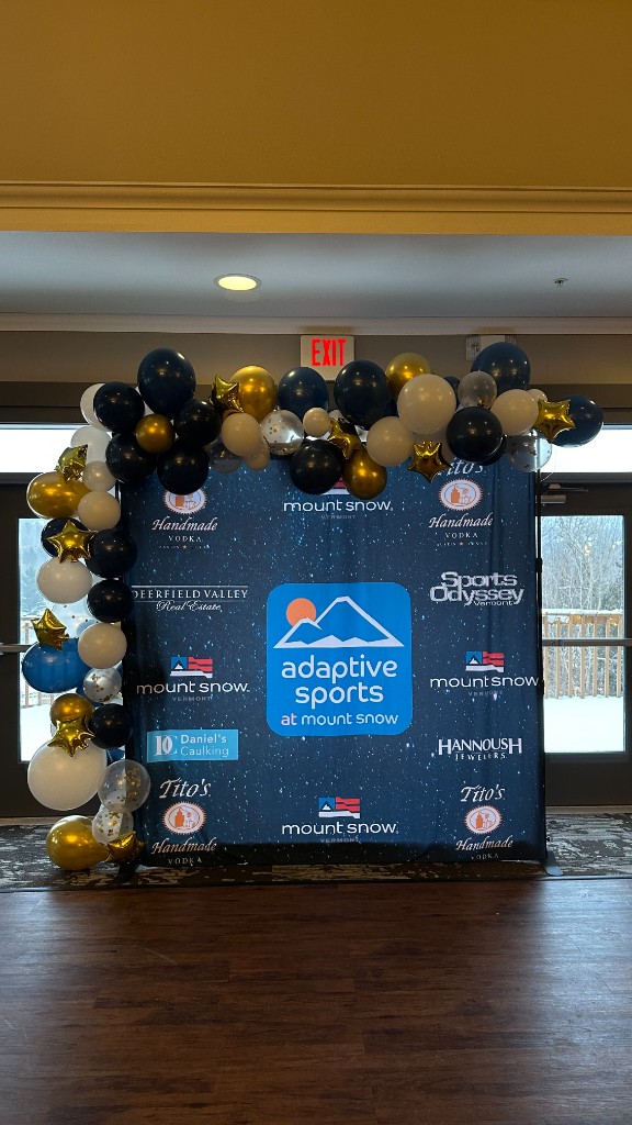 The Adaptive Sports at Mount Snow step-and-repeat, with sponsor logos and a balloon arch.